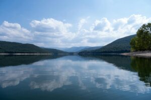 Serene view of a lake in Gavoi, Sardegna, with mountains and clouds reflecting on the water.