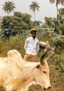 African farmer in a tropical field with cattle grazing, showcasing rural agricultural lifestyle.